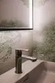 Großer Chrom-Wasserhahn mit schlankem Design, montiert auf einer hellen Oberfläche, umgeben von grünem Wandmuster. Ideal Standard bietet zeitgemäßes Badezimmerzubehör.